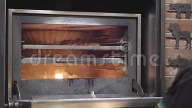 用黑色橡胶手套做饭，用金属工具把一块肉放在烤箱里，用火把。 厨师推鲜多汁的